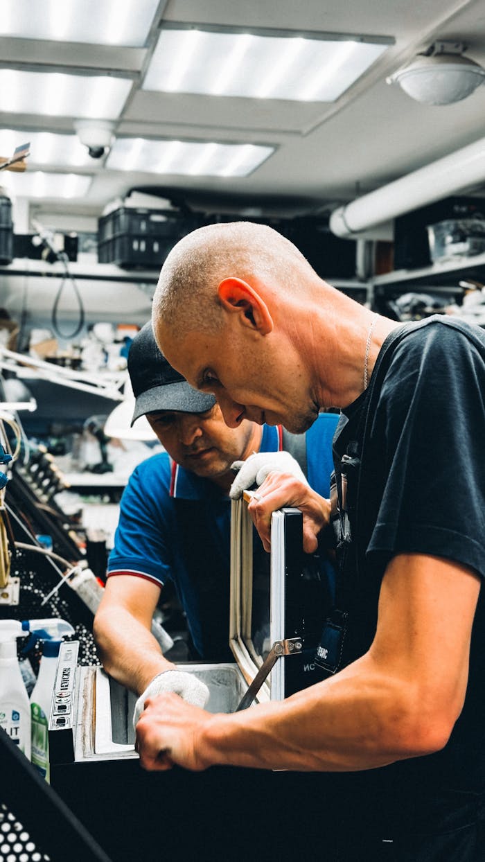 Two male technicians working on electronic repair in a cluttered workshop.